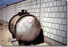 Storage tank found at the Kuwaiti Girls School. Rust-colored fumes eminate from a buleet hole inside the red circle.